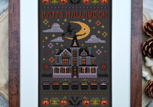 a dark grey piece of fabric with halloween images cross stitched on it in oranges and purples. The piece is framed in a a darkwood frame set on a pale wooden slice of tree trunk.